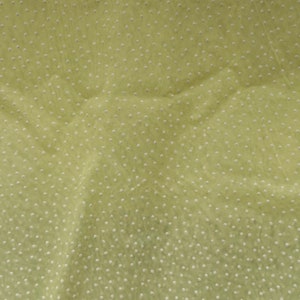 May include: A close-up of a light green fabric with a white polka dot pattern. The fabric is textured and has a slight sheen.
