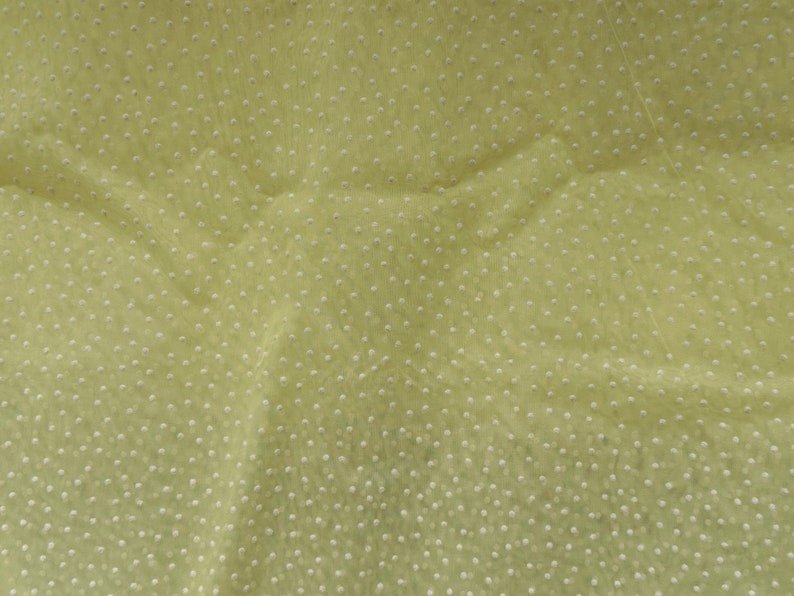 May include: A close-up of a light green fabric with a white polka dot pattern. The fabric is textured and has a slight sheen.