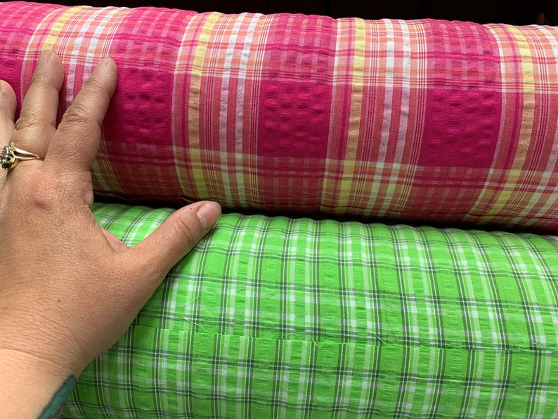 May include: Two rolls of fabric with a plaid pattern. The top roll is pink with white and yellow stripes. The bottom roll is green with white stripes.