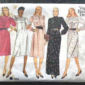 May include: Vintage Vogue Basic Design sewing pattern featuring five dress designs. The illustrations showcase dresses in various colors and styles, including a pink dress with short sleeves, a white dress, a pink dress with a bow, a black dress, and a white dress with red polka dots.
