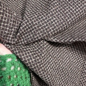 May include: Close-up of a brown and white checkered fabric. The fabric is folded and draped, showing the texture and pattern. A green crocheted sleeve is visible in the lower left corner.