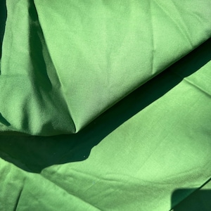 May include: A close-up of a green fabric with a smooth texture. The fabric is folded in half, creating a crease down the middle.