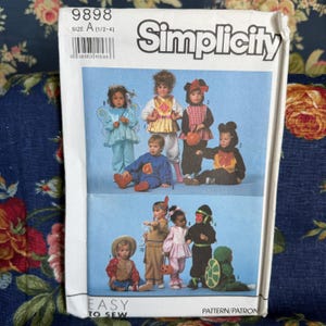 May include: A Simplicity sewing pattern envelope 9898, size A (1/2-4), featuring illustrations of children in various costumes including a fairy, a mouse, a turtle, and a Native American-inspired outfit. The white paper envelope includes text.