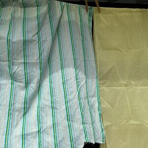 May include: Two pieces of fabric hanging on a clothesline. One piece is a light blue fabric with green, white, and purple stripes. The other piece is a light yellow fabric with white polka dots.