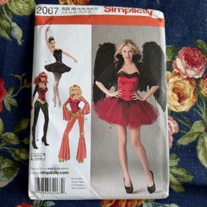 May include: A Simplicity sewing pattern envelope labelled 2067, size R5 14, 16, 18, 20, 22. The front displays illustrations of three costume designs and a photograph of a person wearing a red corset top with a black tulle skirt and black wings.
