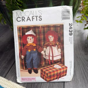 May include: A McCall's Crafts pattern envelope featuring Raggedy Ann and Andy dolls. The dolls are displayed in a box with a plaid pattern. The envelope has the number 2439 and the text "Raggedy Ann & Andy".