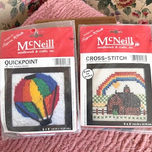 May include: Two McNeill needlework kits. One is a Quickpoint kit with a rainbow balloon design, measuring 6 x 6 inches (15.24 x 15.24 cm). The other is a Cross-Stitch kit with a country rainbow design, measuring 5 x 5 inches (12.70 x 12.70 cm).