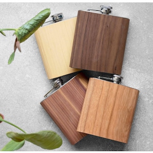 Puede incluir: Cuatro petacas rectangulares de metal con acabados de veta de madera en tonos variados de marrón claro, medio y oscuro. Cada petaca cuenta con un tapón de rosca plateado en la parte superior central, mostrando texturas y vetas naturales.