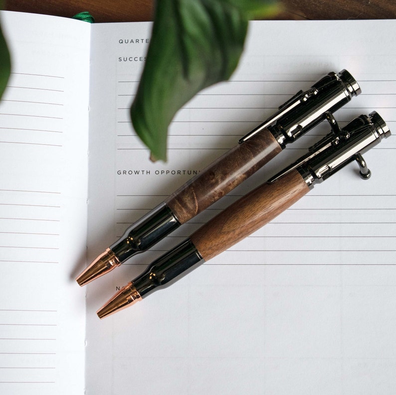 Walnut and Maple Burl Bolt Action Pens photographed on top of a white journal page to show two different available wood variations.