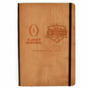 May include: A rectangular notebook with a light brown wood grain cover featuring a black elastic closure. The cover is engraved with the text PLAYOFF SEMIFINAL, PlayStation Fiesta Bowl, and the date DECEMBER 28, 2019, alongside a football icon.