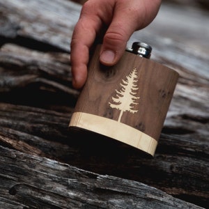 Pode incluir: Uma garrafa de madeira com uma moldura de madeira clara e um design de pinheiro gravado a laser.
