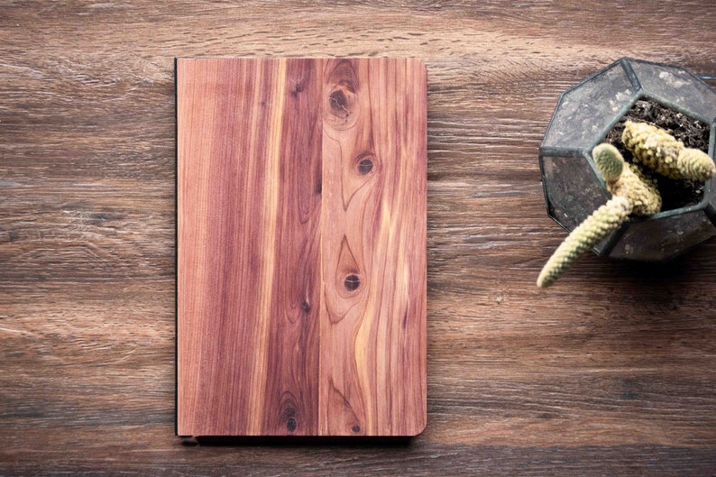 May include: A wooden journal with a natural wood grain finish. The journal is closed and sitting on a wooden surface.