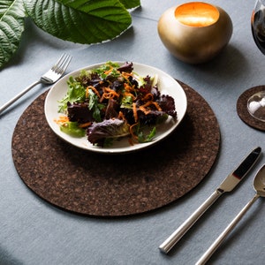 May include: A brown cork round placemat with a white plate containing a salad of mixed greens, red lettuce, and shredded carrots. A silver fork and knife are on the table.