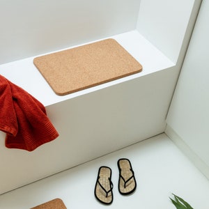 Op de afbeelding: Een witte badkamer met een kurken badmat, een rode handdoek en twee zwarte slippers.