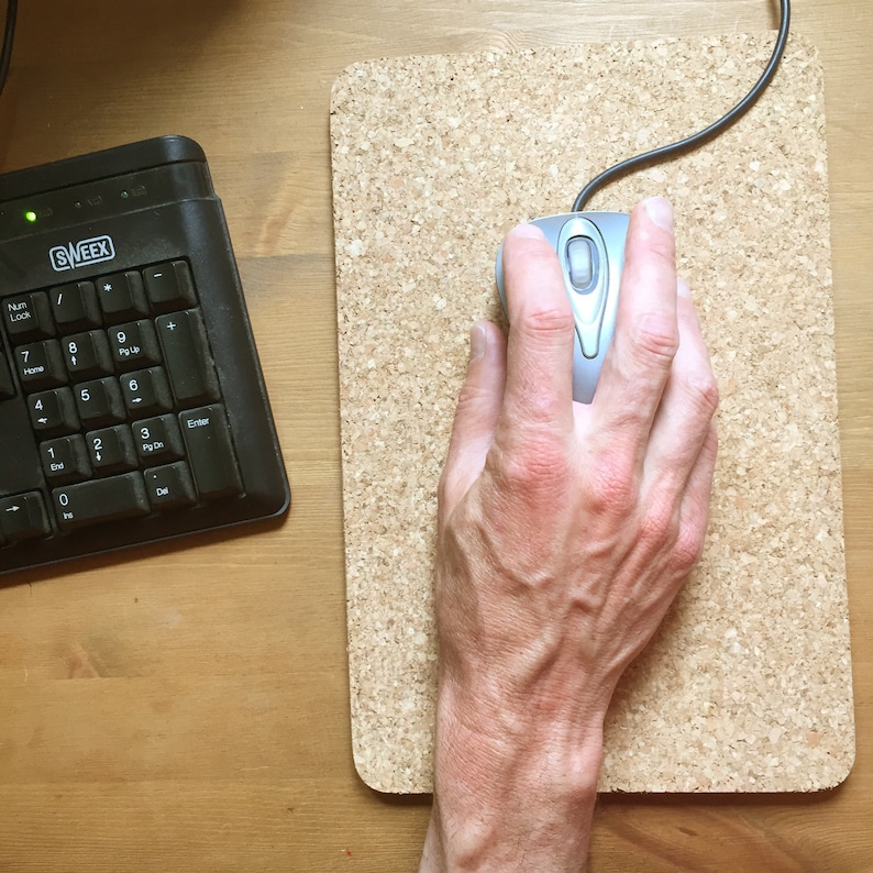 May include: A hand using a silver computer mouse on a cork mousepad.