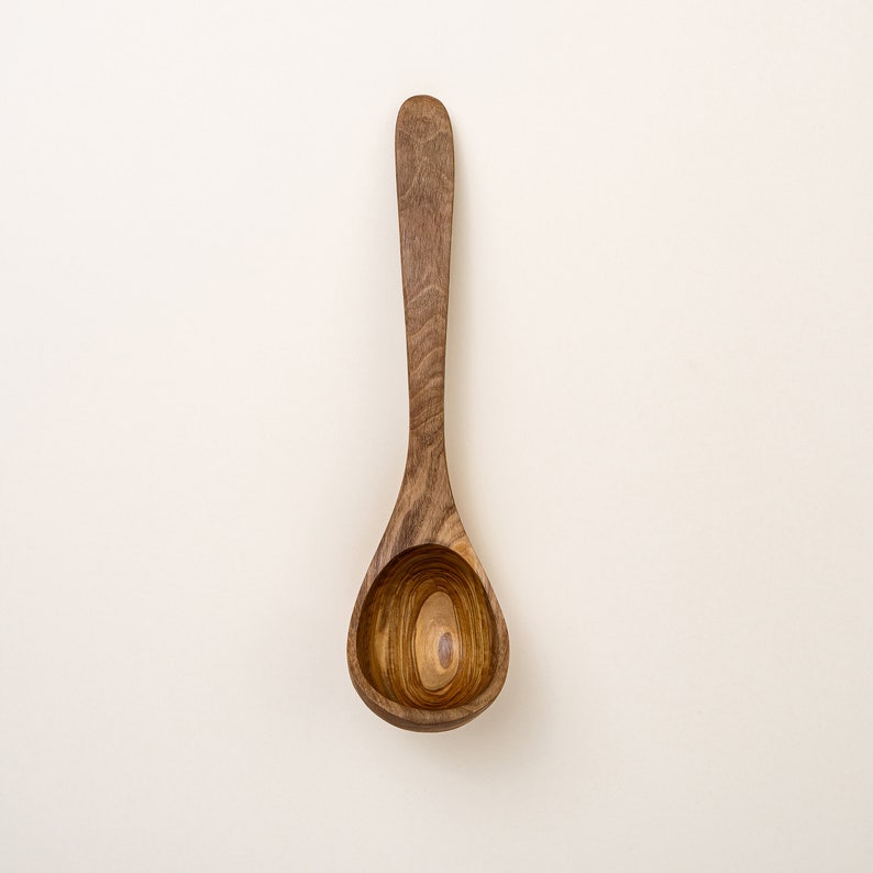 May include: A wooden ladle with a brown finish and a natural wood grain. The ladle has a rounded bowl and a long handle.