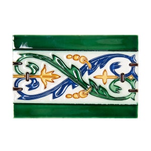 May include: Rectangular ceramic tile with a white background and a decorative border. The border features green, blue, and gold floral patterns. The top and bottom edges are solid green.