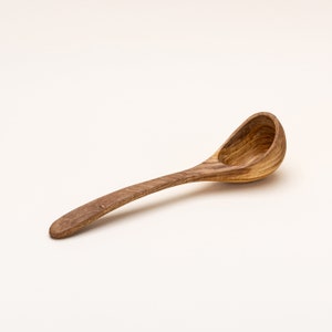 May include: A wooden ladle with a long handle and a rounded bowl. The ladle is made of light brown wood with dark brown grain patterns.