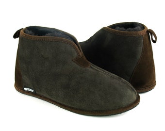 Op de afbeelding: Een paar bruine suède pantoffels met een voering van schapenvacht. De pantoffels hebben een gesloten neus en een slip-on ontwerp.