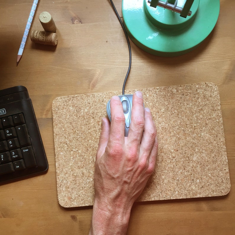 May include: A hand using a silver computer mouse on a cork mousepad.