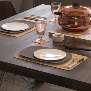 Könnte beinhalten: Ein Holztisch mit zwei Gedecken, jedes mit einem weißen Teller, einem grauen ovalen Teller, einem rosa Glas und einem Korkuntersetzer. Ein Kupfertopf mit einem Korkuntersetzer steht auf dem Tisch, zusammen mit einer kleinen weißen Schüssel und einem Rosmarinzweig.