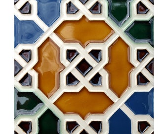 May include: Square ceramic tile with a geometric pattern. The design features interlocking shapes in shades of blue, green, and gold, outlined with white. Dark brown accents add depth to the design.