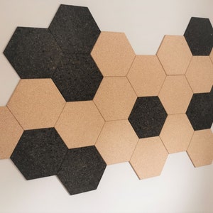 May include: A wall covered in cork hexagon tiles, half are black and half are natural cork.