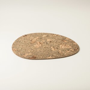 Pu&ograve; includere: Un sottobicchiere in sughero marrone chiaro con un motivo naturale e organico. Il sottobicchiere &egrave; di forma ovale e ha un bordo leggermente irregolare.