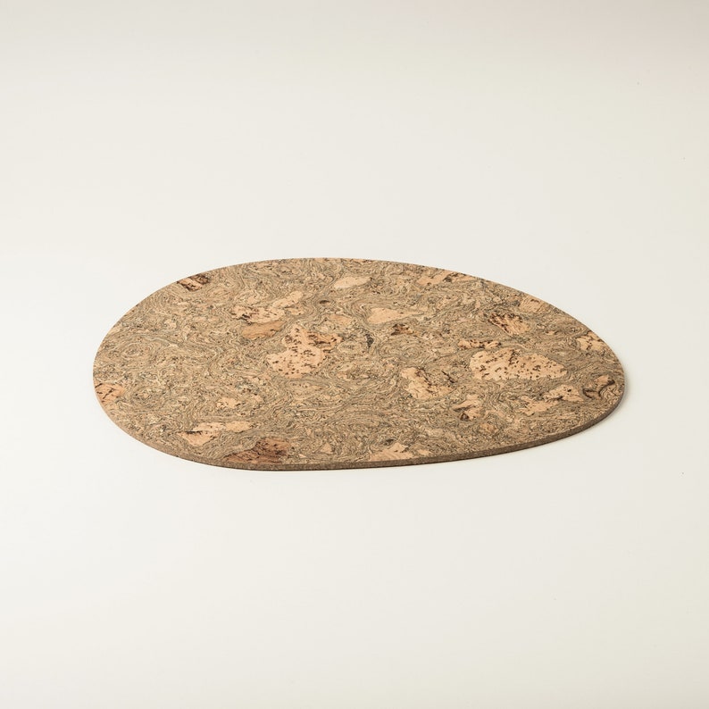 Pu&ograve; includere: Un sottobicchiere in sughero marrone chiaro con un motivo naturale e organico. Il sottobicchiere &egrave; di forma ovale e ha un bordo leggermente irregolare.