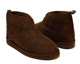 Op de afbeelding: Een paar bruine suède pantoffels met een voering van schapenvacht. De pantoffels hebben een gesloten neus en een slip-on ontwerp.