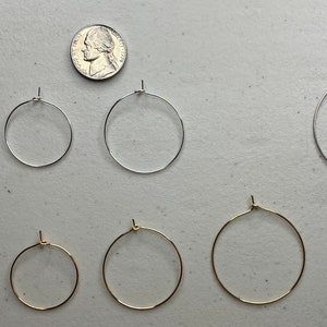 Puede incluir: Una variedad de pendientes de aro en tonos plateados y dorados, exhibidos sobre una superficie clara. Se incluye una moneda para mostrar la escala. Los pendientes tienen un dise&ntilde;o simple y cl&aacute;sico, adecuados para el uso diario. Medidas en cent&iacute;metros.