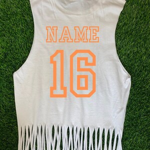 Pu&ograve; includere: Maglietta bianca senza maniche con orlo sfrangiato. Sul retro della maglietta sono stampate le parole "NAME" e il numero "16" in arancione.