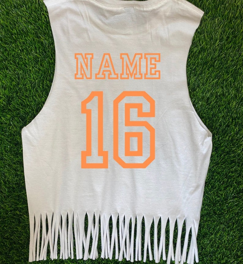 Pu&ograve; includere: Maglietta bianca senza maniche con orlo sfrangiato. Sul retro della maglietta sono stampate le parole "NAME" e il numero "16" in arancione.