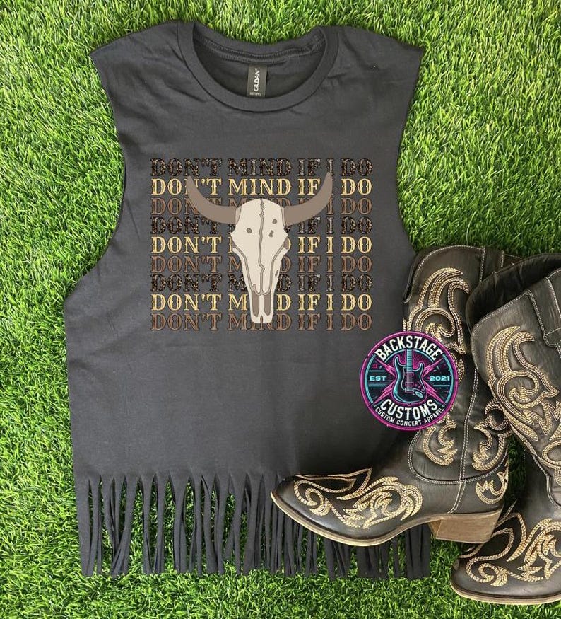 May include: Black sleeveless shirt with a fringe hem. The shirt features a brown and white cow skull graphic with the text "Don't Mind If I Do" repeated multiple times.