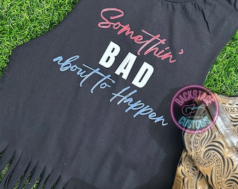 Könnte beinhalten: Schwarzes ärmelloses Shirt mit ausgefranstem Saum. Das Shirt hat den Text "Somethin' BAD about to happen" in Rot, Weiß und Blau aufgedruckt.