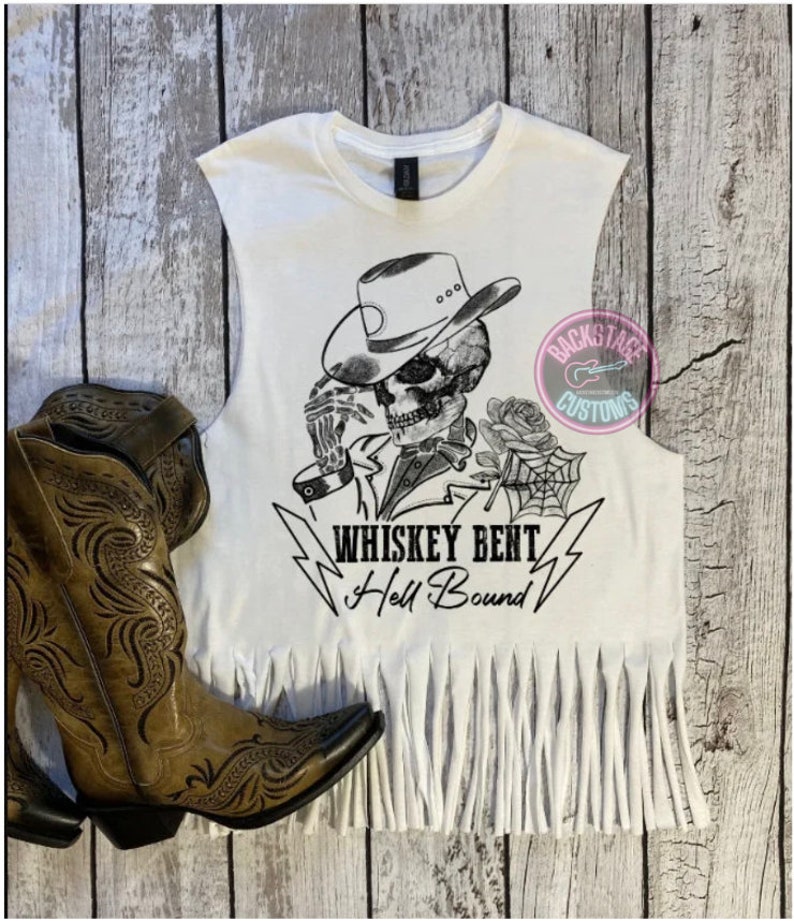 May include: White sleeveless shirt with a black and white graphic of a skeleton wearing a cowboy hat and holding a rose. The text "Whiskey Bent Hell Bound" is printed below the graphic.
