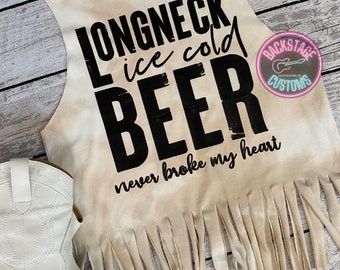 May include: A beige sleeveless shirt with a frayed hem. The shirt has black text that reads "Longneck ice cold beer never broke my heart". The shirt also has a small pink and black logo that reads "Backstage Customs".
