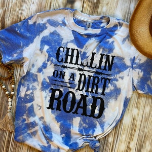 May include: A blue and white tie-dye t-shirt with the text "Chillin on a Dirt Road" in black lettering.