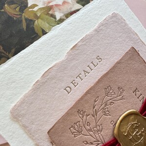 Op de afbeelding: Een elegante briefpapier set met een bloemenontwerp en het woord "DETAILS" in reliëf op een roze kaart. Een gouden waszegel en bordeauxrood lint voegen een vleugje luxe toe. Bevat een bloemenprint en wit getextureerd papier.