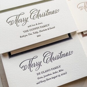 May include: Off-white textured cardstock holiday greeting cards with dark green and black ink. The cards feature the text Merry Christmas, family names, and the year 2021 in a mix of elegant script and serif fonts, framed by thin colored borders.