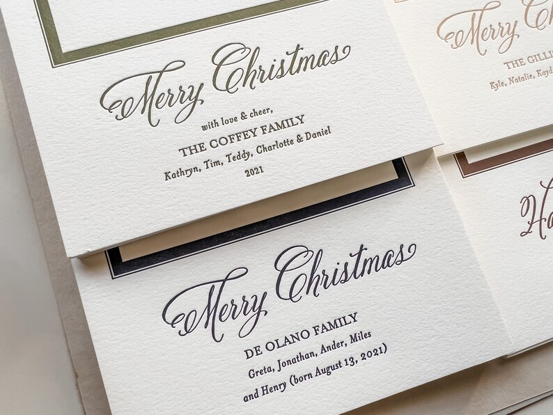 May include: Off-white textured cardstock holiday greeting cards with dark green and black ink. The cards feature the text Merry Christmas, family names, and the year 2021 in a mix of elegant script and serif fonts, framed by thin colored borders.