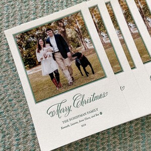 May include: A stack of rectangular holiday cards featuring a photograph of two adults, an infant, and a black dog outdoors. The text reads Merry Christmas, THE SCHIFFMAN FAMILY, Kenneth, Lauren, Anne Clare, and Rex, and the year 2019.
