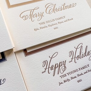 May include: Off-white textured holiday cards with gold and brown ink. One card reads Merry Christmas, The Gillis Family, Kyle, Natalie, Kaydence, Bryce, and Brock 2021. Another card reads Happy Holidays, The Young Family, Joe, Molly, Shaw, Hank, and Daisy 2021.
