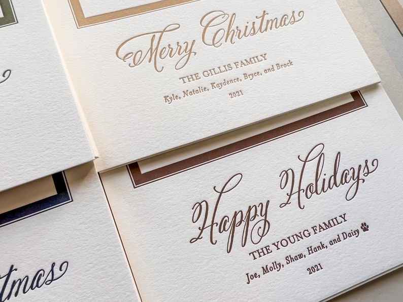 May include: Off-white textured holiday cards with gold and brown ink. One card reads Merry Christmas, The Gillis Family, Kyle, Natalie, Kaydence, Bryce, and Brock 2021. Another card reads Happy Holidays, The Young Family, Joe, Molly, Shaw, Hank, and Daisy 2021.