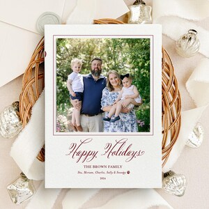 May include: A rectangular holiday greeting card featuring a centered photograph of a family of four outdoors. Below the photo, the text reads: Happy Holidays, THE BROWN FAMILY, Stu, Miriam, Charlie, Sally & Snoopy, and 2024 in dark red ink.