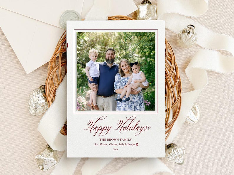 May include: A rectangular holiday greeting card featuring a centered photograph of a family of four outdoors. Below the photo, the text reads: Happy Holidays, THE BROWN FAMILY, Stu, Miriam, Charlie, Sally & Snoopy, and 2024 in dark red ink.