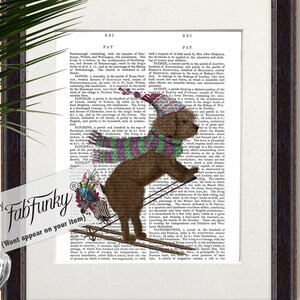Può includere: Un cane marrone con una sciarpa rosa e verde e un cappello rosso sta sciando giù per una collina innevata. Il cane tiene i bastoncini da sci ed è circondato da una pagina di dizionario vintage con testo sulla città di Patrington, in Inghilterra.