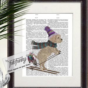 Könnte beinhalten: Gerahmter Kunstdruck mit einem Hund, der auf einer alten Wörterbuchseite Ski fährt. Der Hund trägt eine lila-weiße Mütze, einen gestreiften Schal und Handschuhe. Ein Zebra mit Blumen ist an den Skiern befestigt. Der Rahmen ist dunkelbraun.