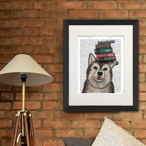 May include: A framed print of a brown and white husky dog with a stack of books on its head. The print is on a white background with black text. The print is hanging on a brick wall above a brown leather sofa.
