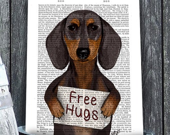 Puede incluir: Un perro salchicha negro y marrón sosteniendo un cartel que dice "Free Hugs". El perro está de pie frente a una página de libro vintage con texto.
